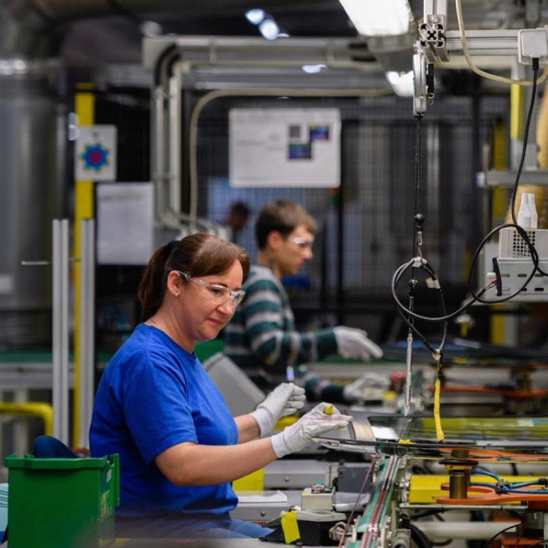 Mujer y hombre en línea de producción para vidrio automotriz.